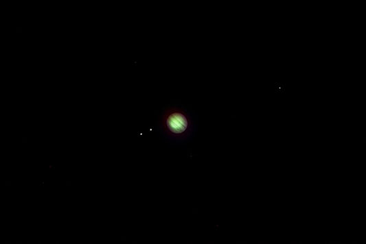 A striking night view of Jupiter with its moons captured in vibrant detail against a black sky.
